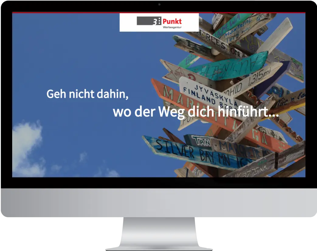 An iMac displaying the webdesign for 3punkt. Hero section with a large image of traffic signs and the sentence "don't walk where the road leads you..."